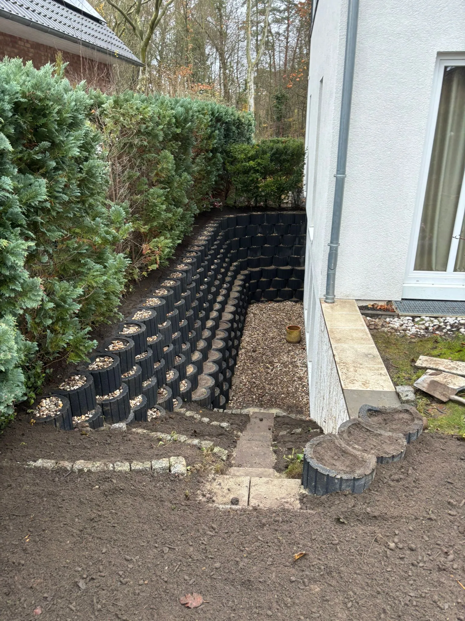 Geschwungene Pflanzsteinmauer entlang eines Hangs neben einem Wohnhaus